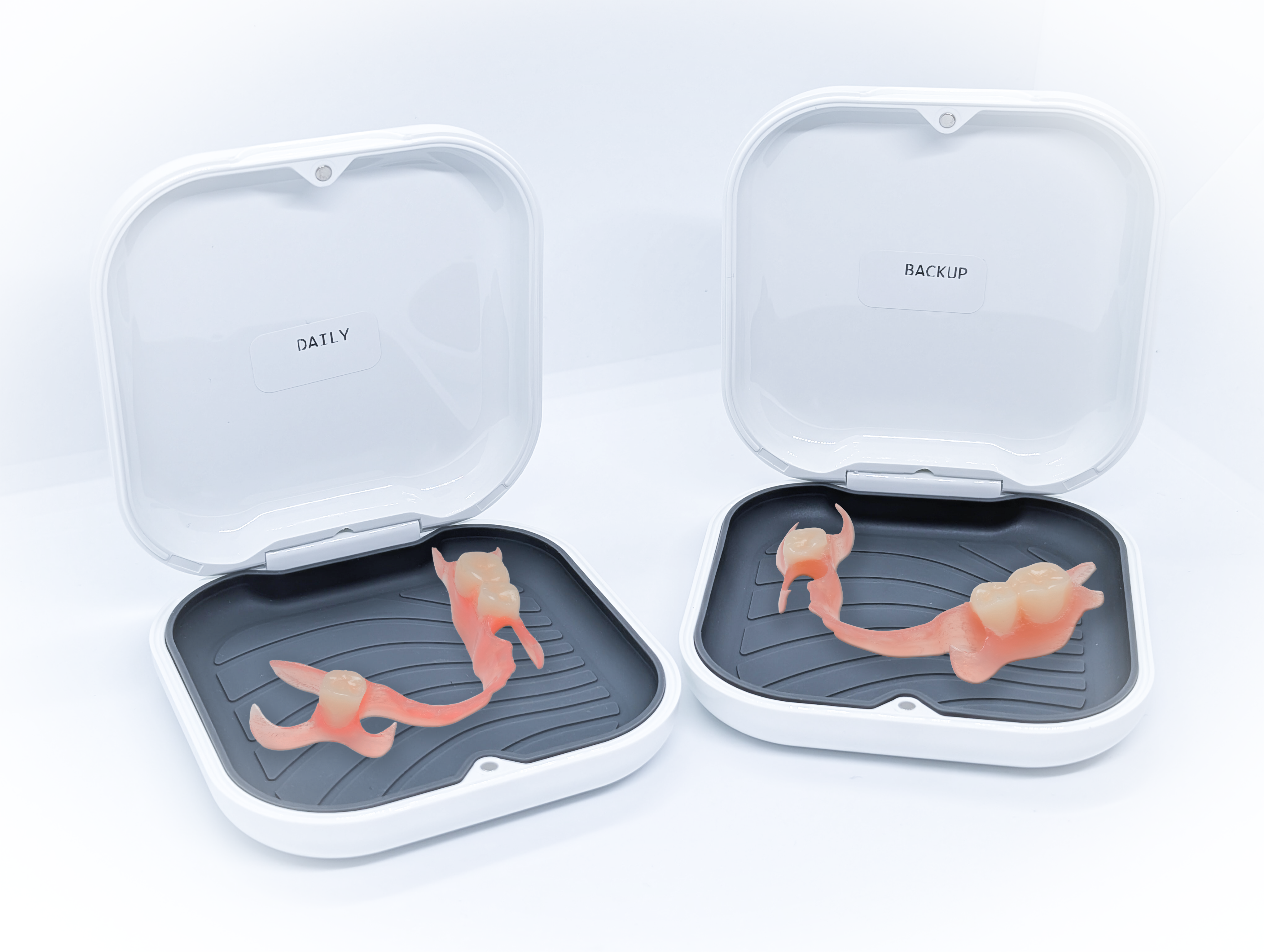 Two white cases with partial dentures inside on a light gray background
